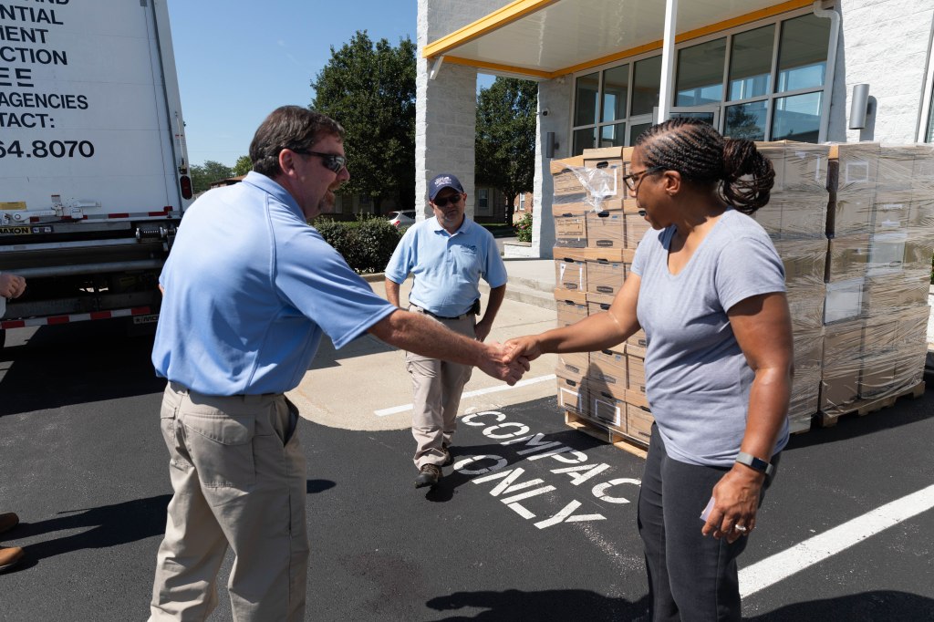 Environmental Scientist Advisor Brian Bentley shakes hands with Sharon Stone, farmer liaison of the Woodhill International Market, after he and other KGRS employees deliver boxes for the market to use. 