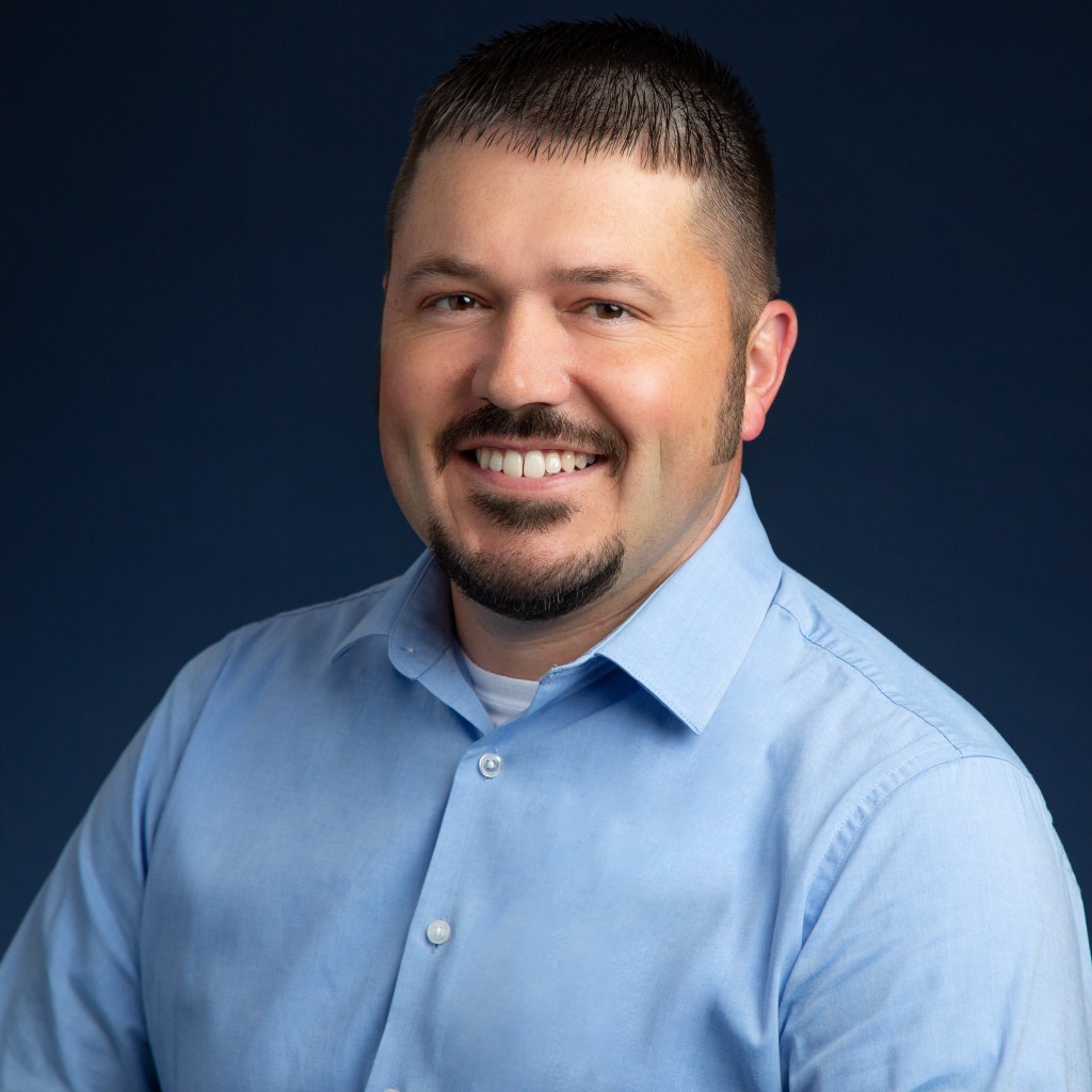 Young man with dark hair in blue button up shirt. 