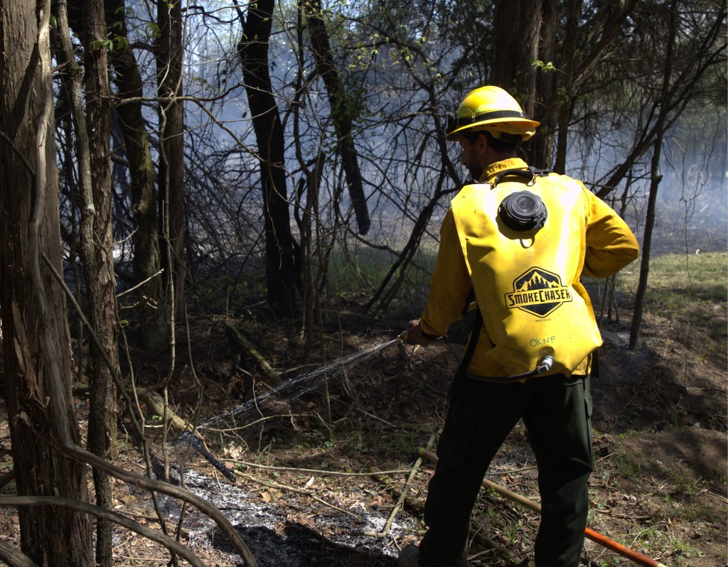 Man putting water on smoldering fire. 