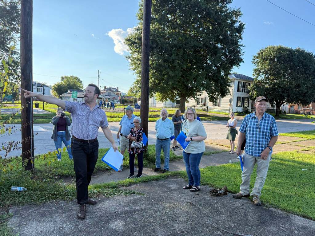 Man pointing at buildings as onlookers look at properties.